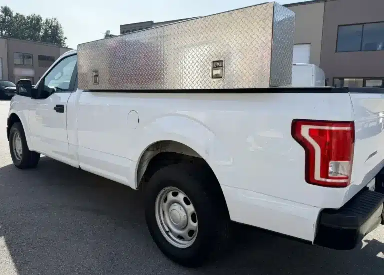 Metal toolbox mounted across the bed of a white pickup truck